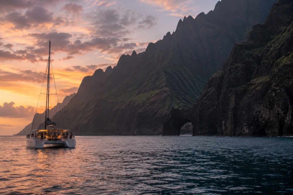 A dinner cruise catamaran anchored in calm evening water near the Napali shoreline
