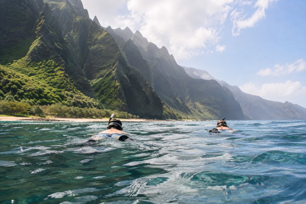 Snorkellers floating over a clear reef near the Napali Coast with cliffs behind