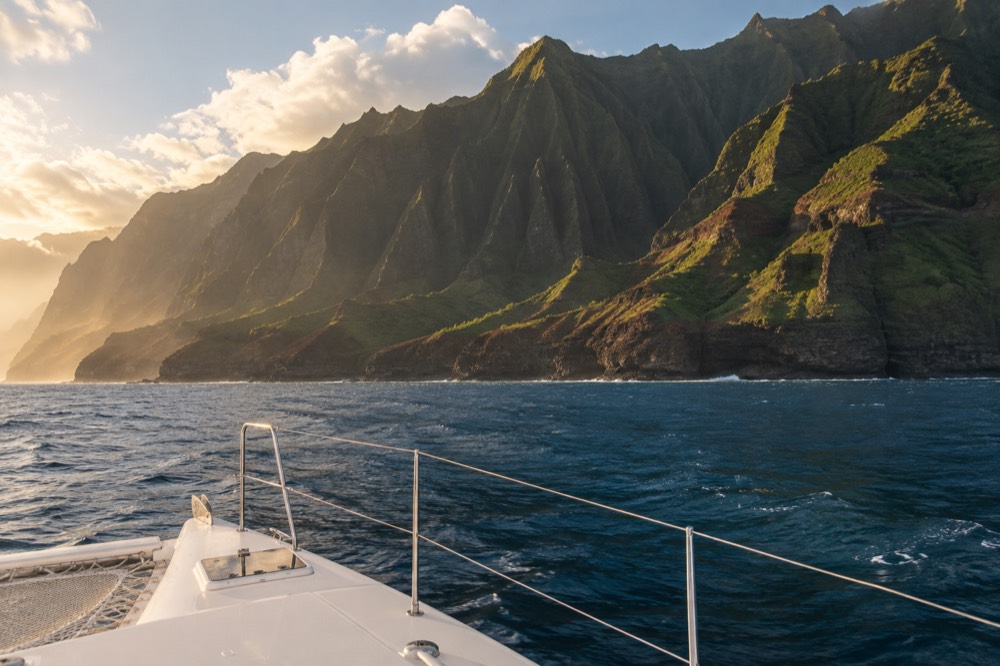 A power catamaran cruising close to the sea cliffs in golden evening light