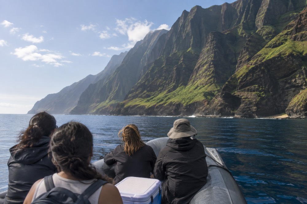 A rigid inflatable raft cruising along the sea cliffs of the Napali Coast on calm water.