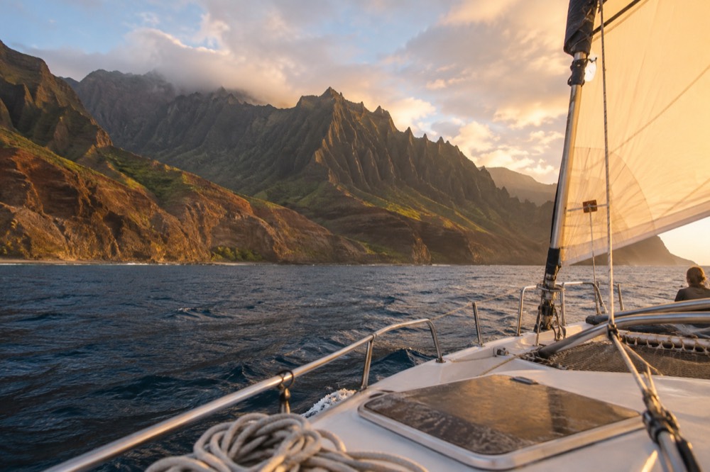 A catamaran under way on the Napali Coast in warm late afternoon light near the sea cliffs