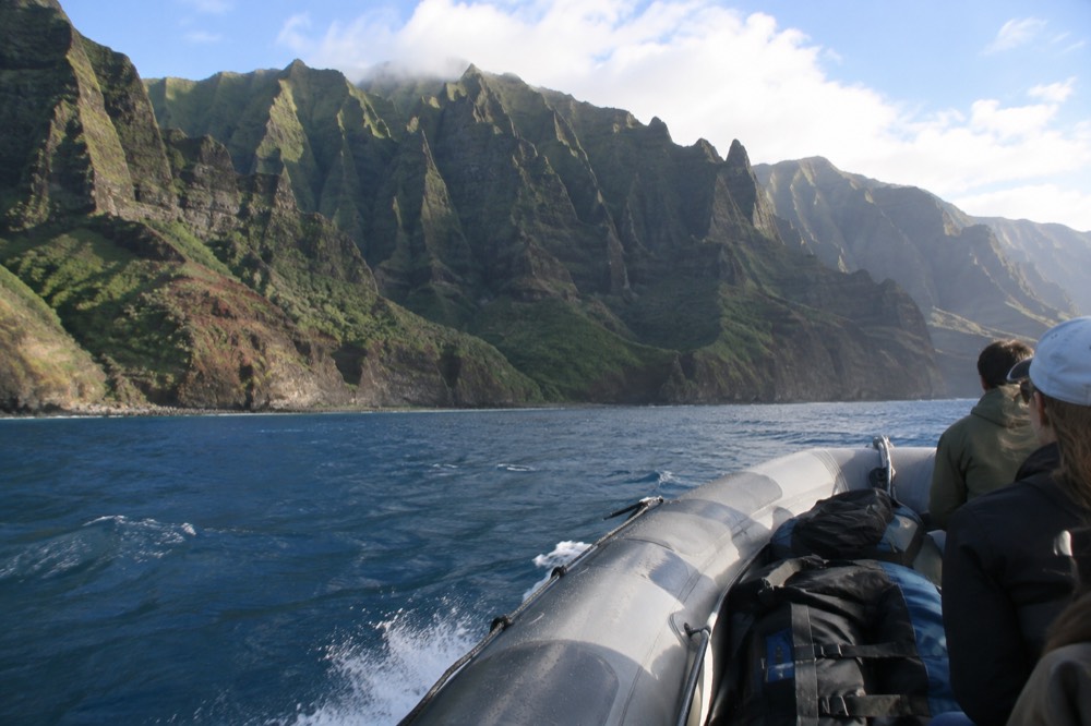 A rigid inflatable raft cruising along a tall green sea cliff toward a snorkel stop