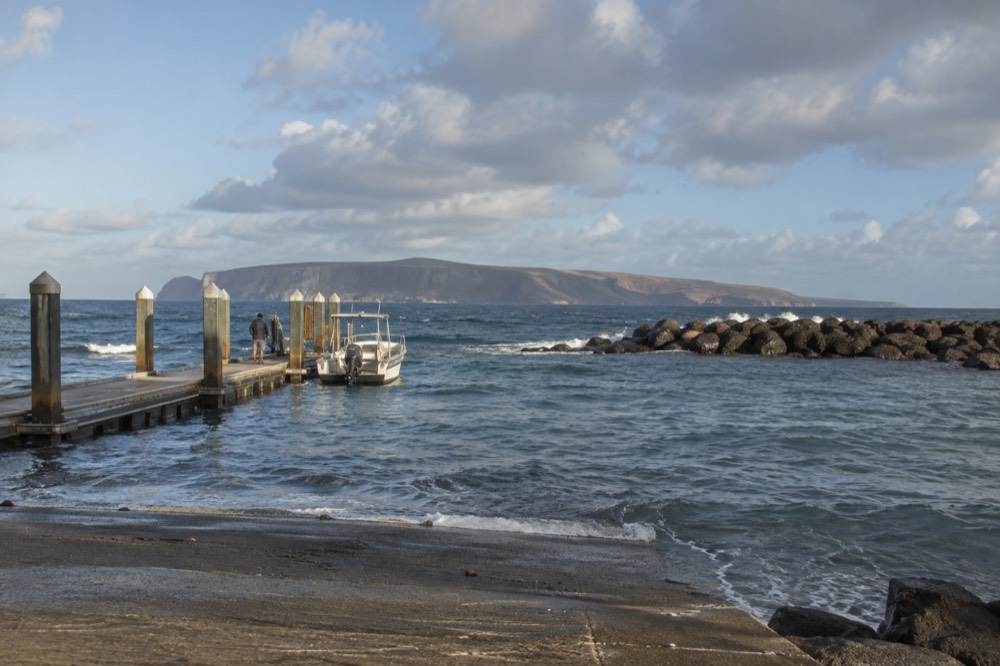 Arid low-lying Niihau island stretching along the horizon under scattered clouds