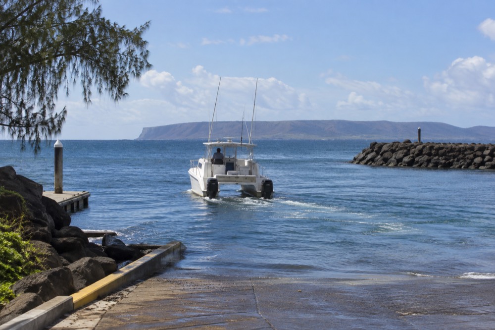 A power catamaran cruising on open channel water with a distant low island on the horizon
