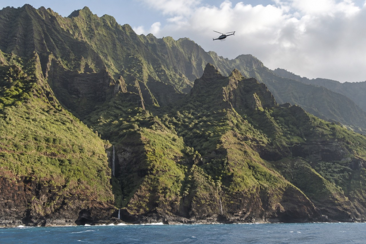 A helicopter flying above green sea cliffs on a Hawaiian coastline