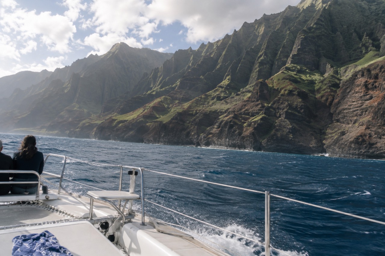 A boat crossing open water toward the steep green cliffs of the Napali Coast on Kauai.