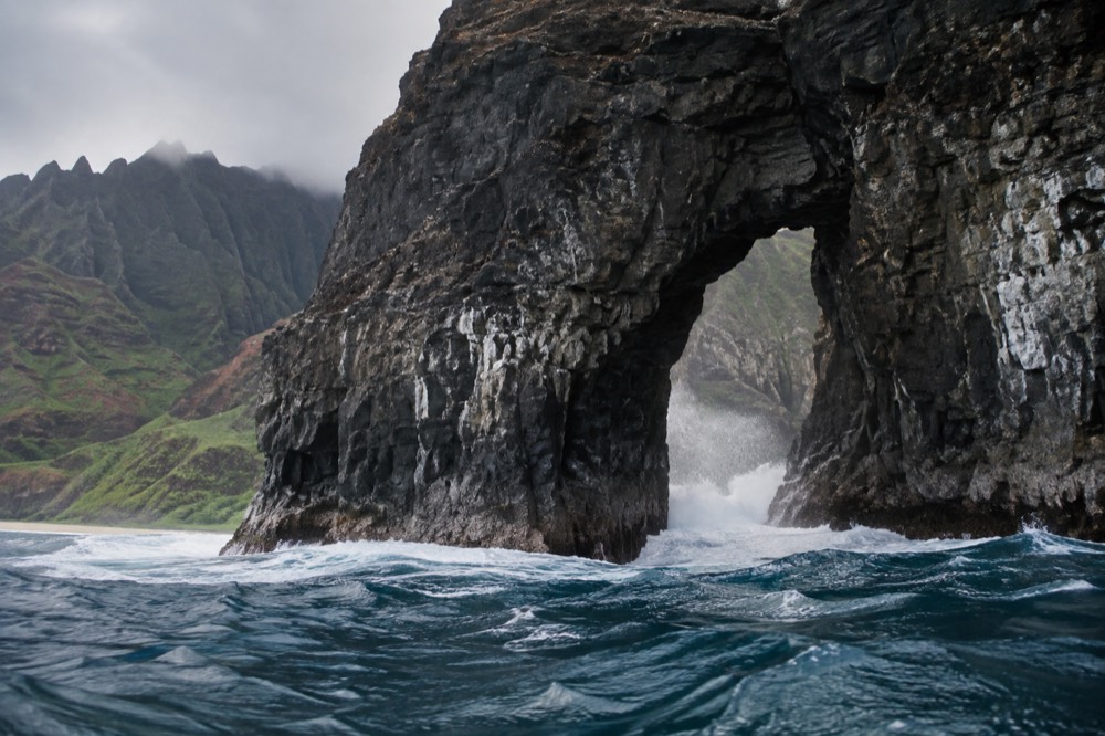 A tall sea arch in a cliff with waves passing through it along a wild coastline