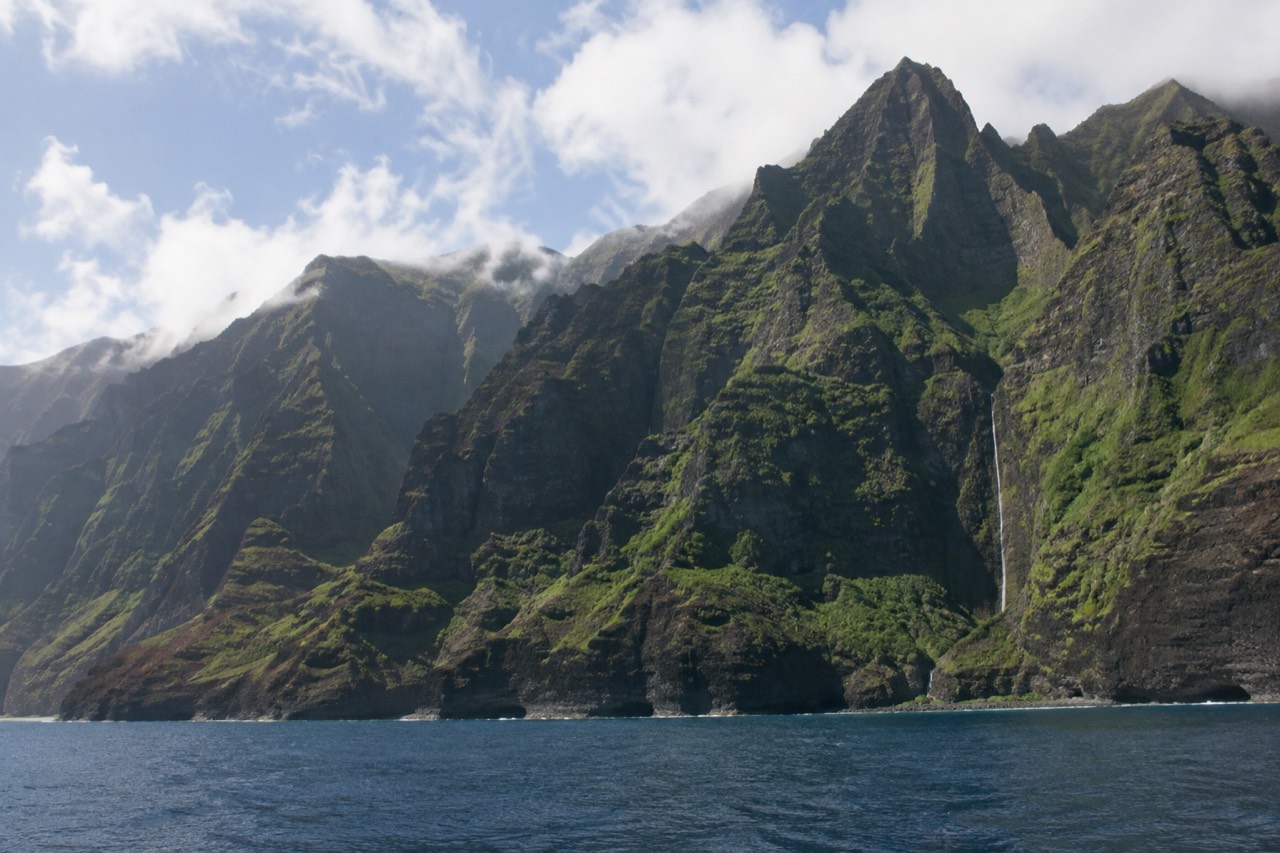 Green sea cliffs of the Napali Coast rising above calm blue water near Kauai