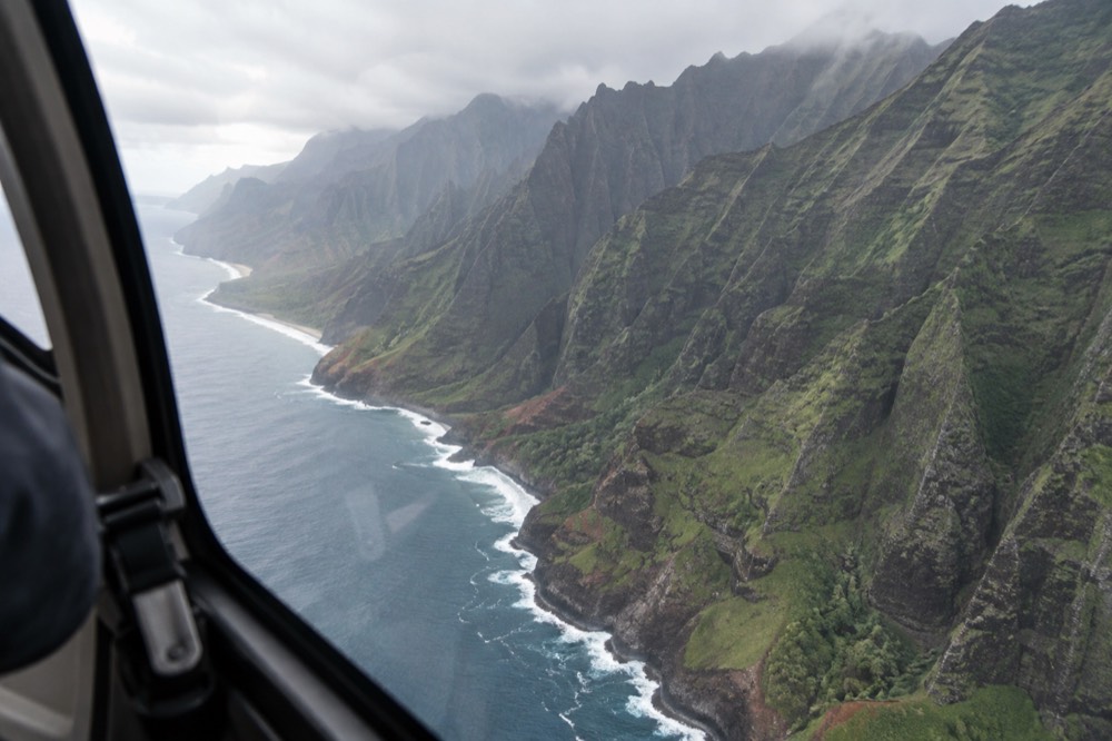 A helicopter cabin interior view over rugged green mountain ridges