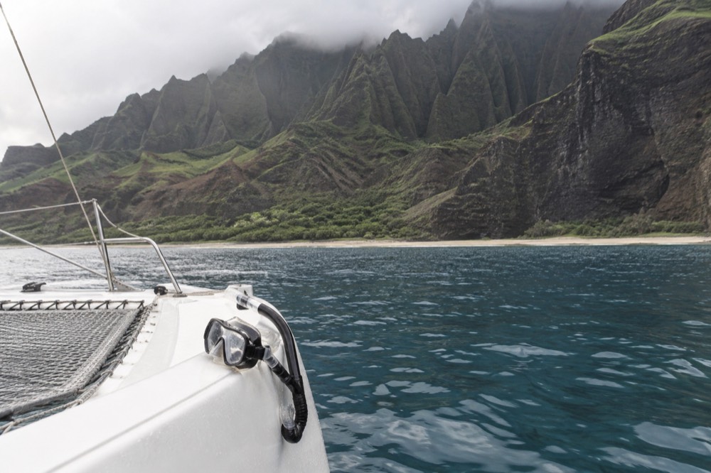 A catamaran anchored near a reef in clear turquoise water below steep cliffs