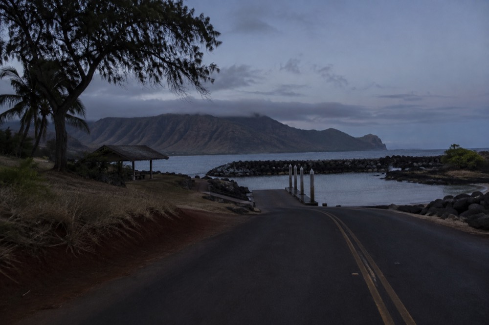 An empty two-lane coastal road on Kauai at dawn with mist over the ridges
