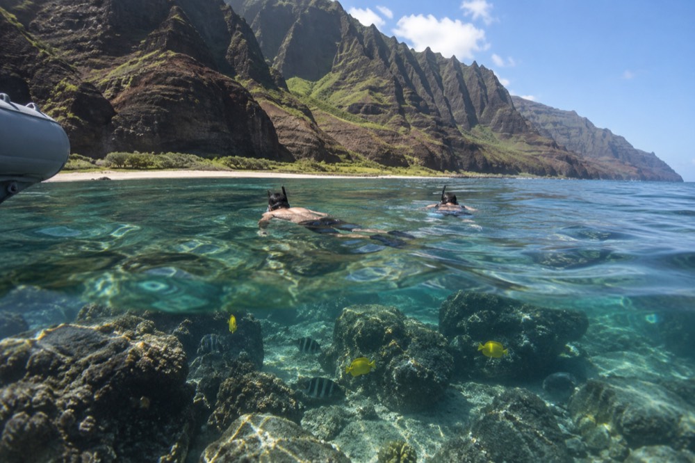 Snorkellers floating over a shallow reef with fish visible near the boat