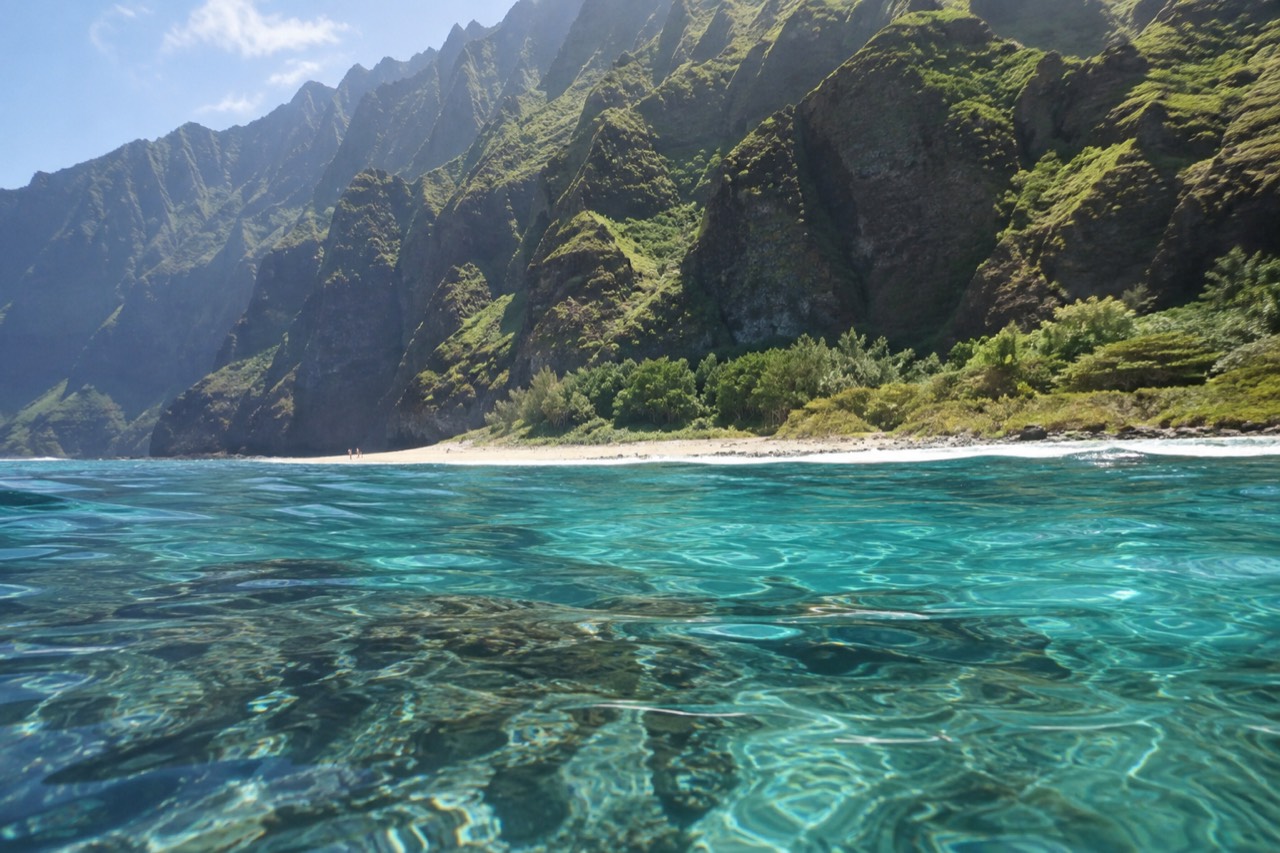 Clear turquoise water over a coral reef along a steep volcanic coastline