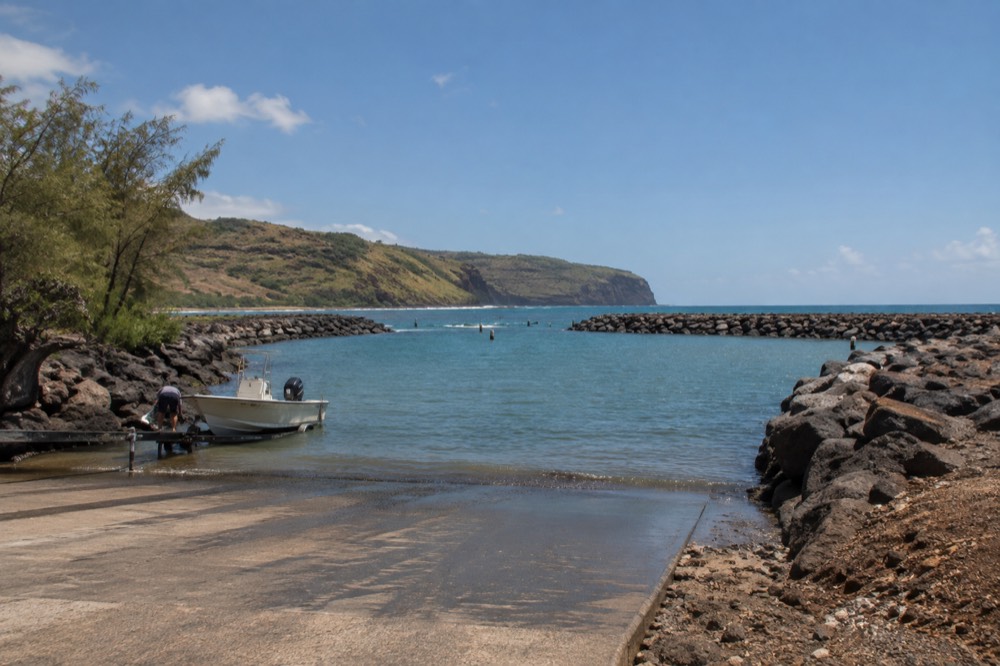 A narrow two-lane coastal road curving along a green Hawaiian hillside above the ocean