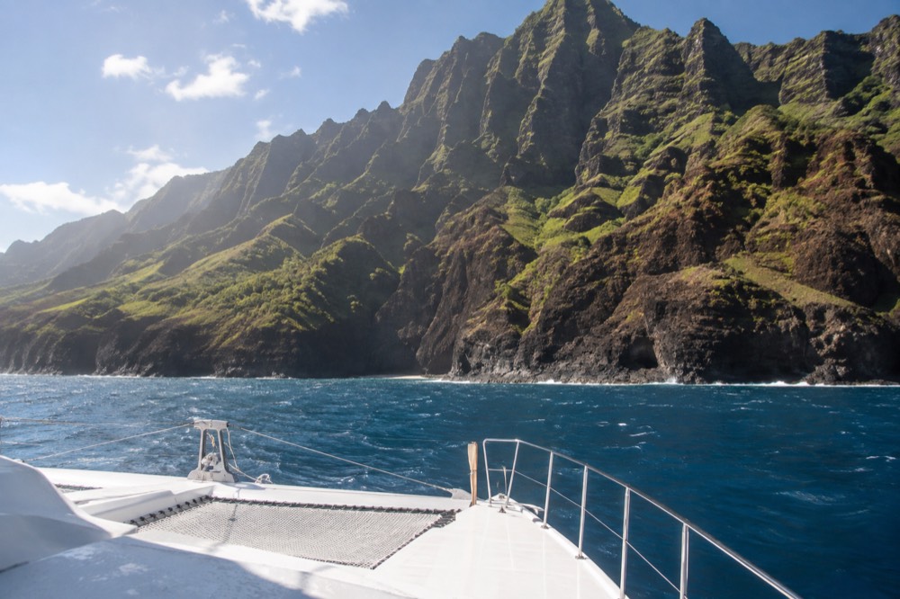 A power catamaran cruising past tall green sea cliffs along a rugged coastline
