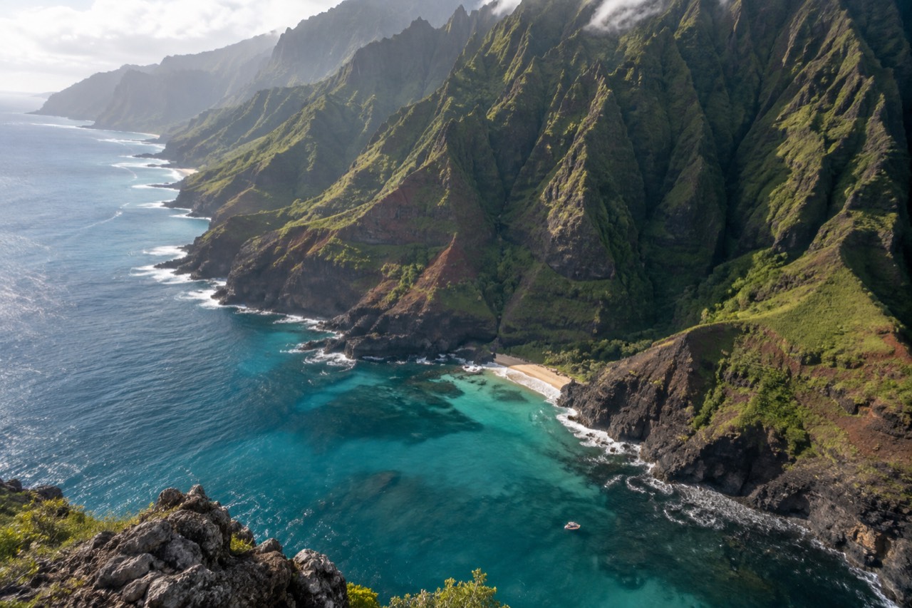 Aerial view of the Napali Coast's green cliffs plunging into turquoise water with a small boat below