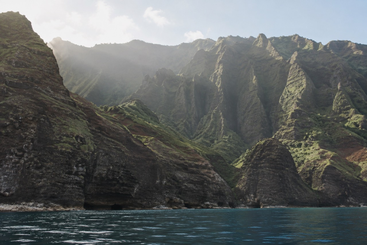 Tall green sea cliffs rising from calm Pacific water along the Napali Coast of Kauai