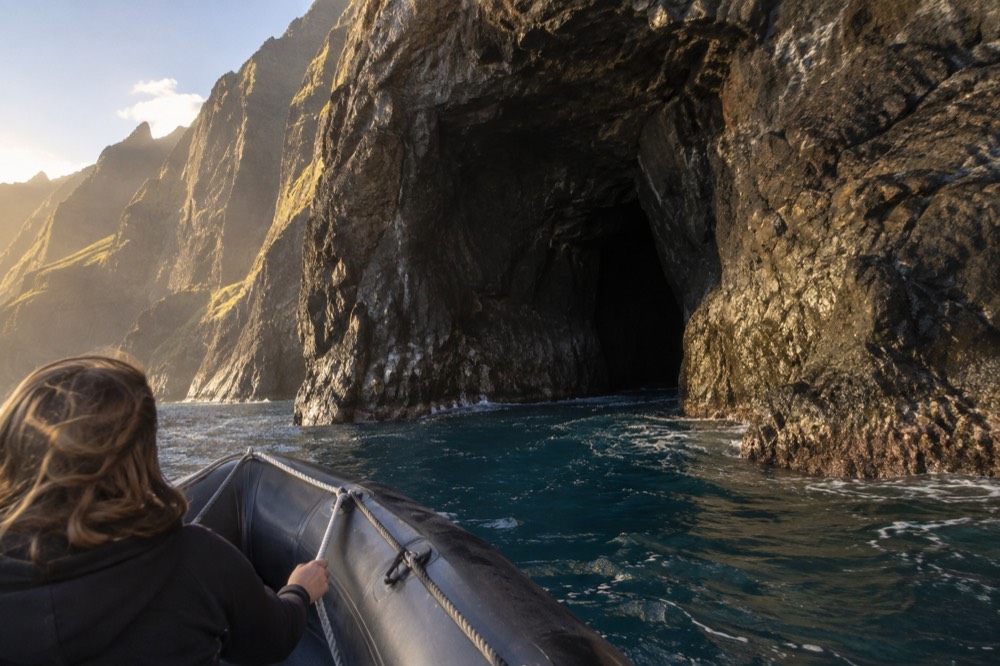 A small rigid-hull inflatable raft cruising close to a dark sea cave entrance