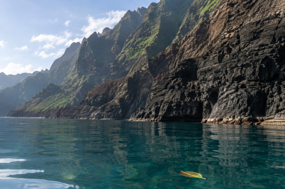 Glassy July morning water mirrors the green Napali sea cliffs of Kauai