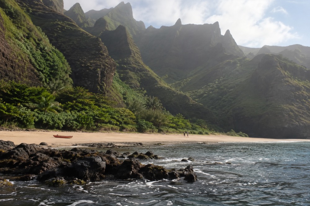 Towering green cliffs and a narrow valley meeting the ocean along the Napali Coast