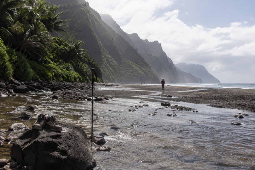 A stream crossing a dark sand beach at the base of a steep green valley