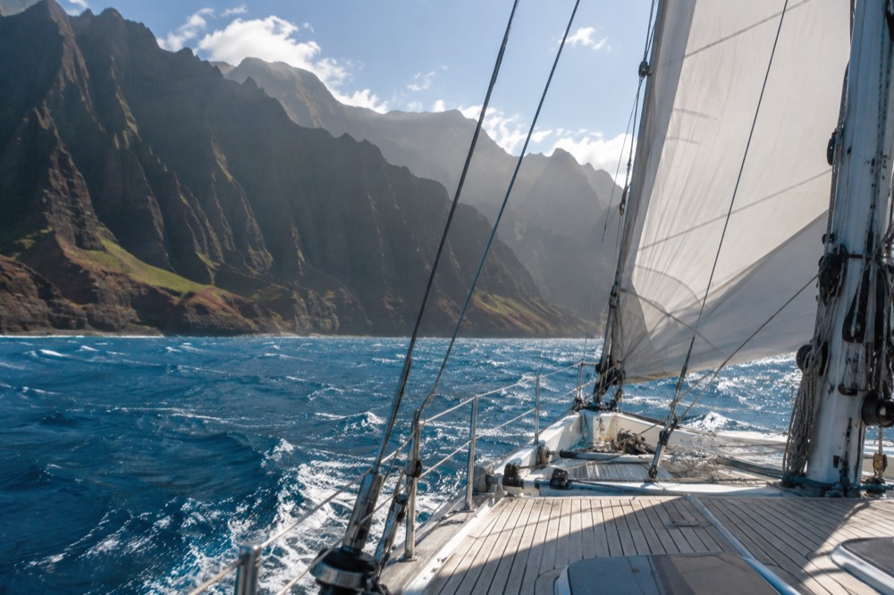 A sailing catamaran on open water with sea cliffs in the far distance