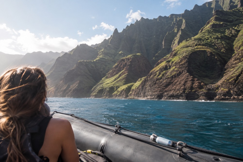 A rigid-hull inflatable raft cruising close to tall green sea cliffs in calm summer water