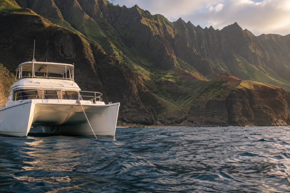 A power catamaran moored near a rocky coastline with green cliffs