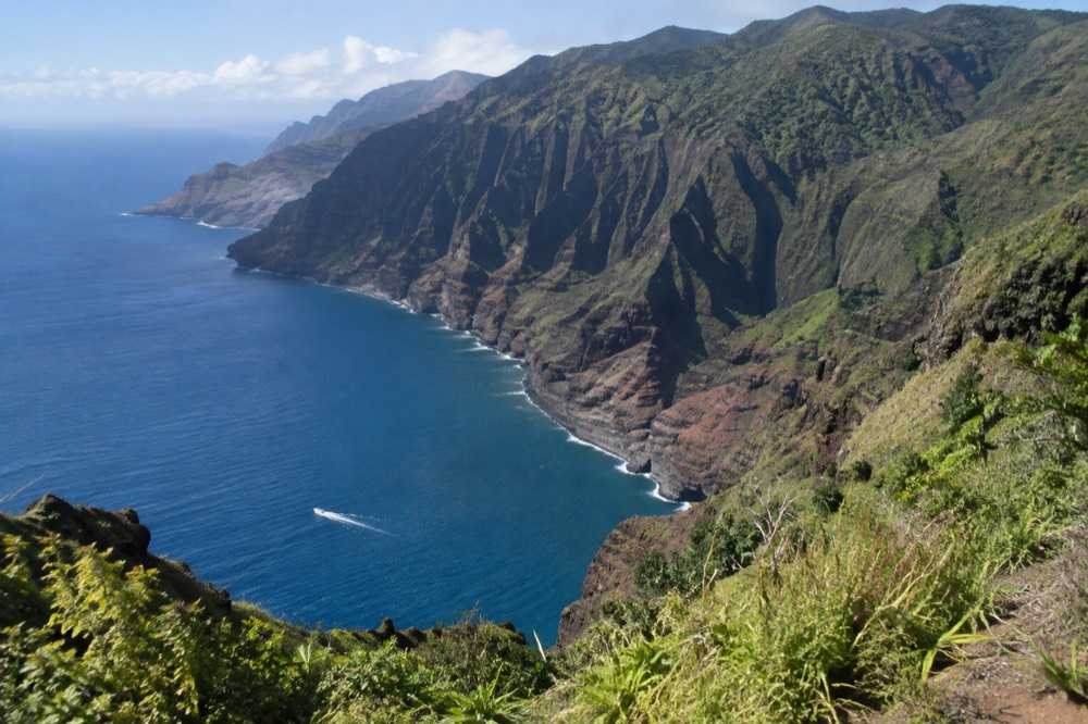 Napali sea cliffs rising from calm blue water with a small boat passing below