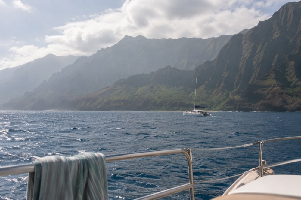 A catamaran under way on open water with folded green ridges along the horizon