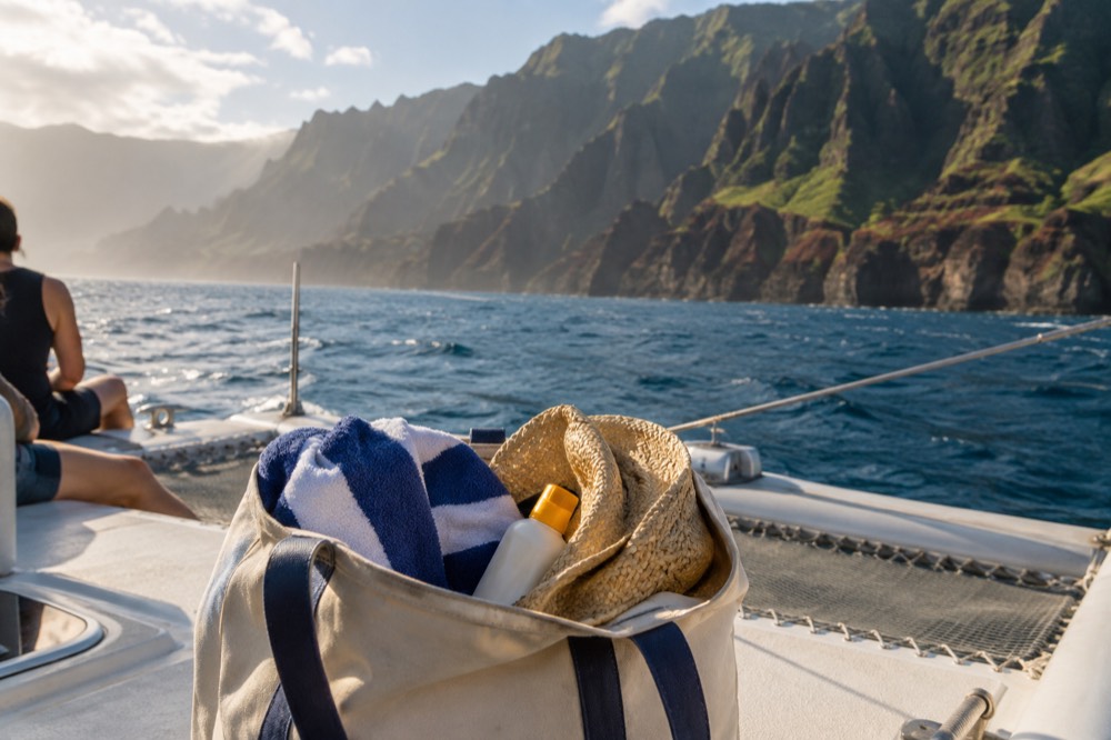 A canvas bag with a towel, sunscreen and a hat on a boat deck