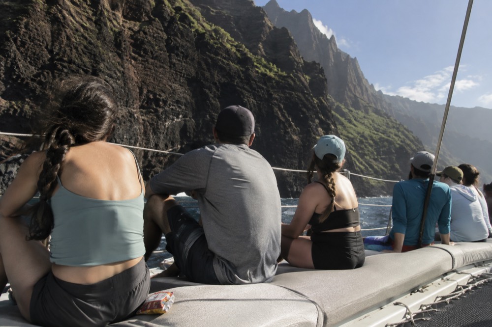 A catamaran with passengers seated along its deck near sea cliffs