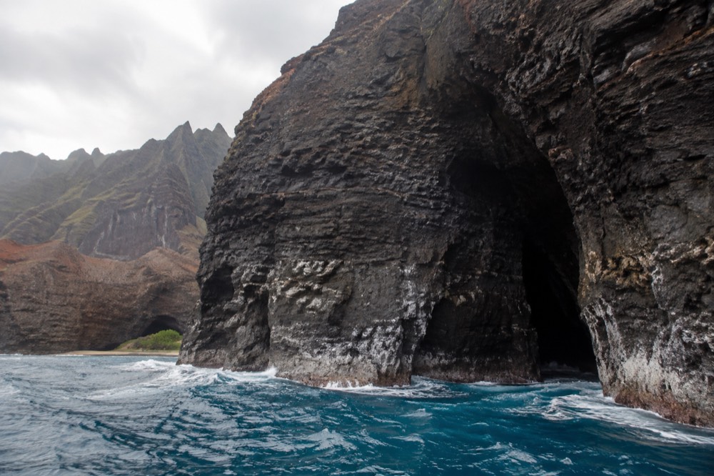 A dark sea cave opening in a cliff face with blue ocean water at its mouth