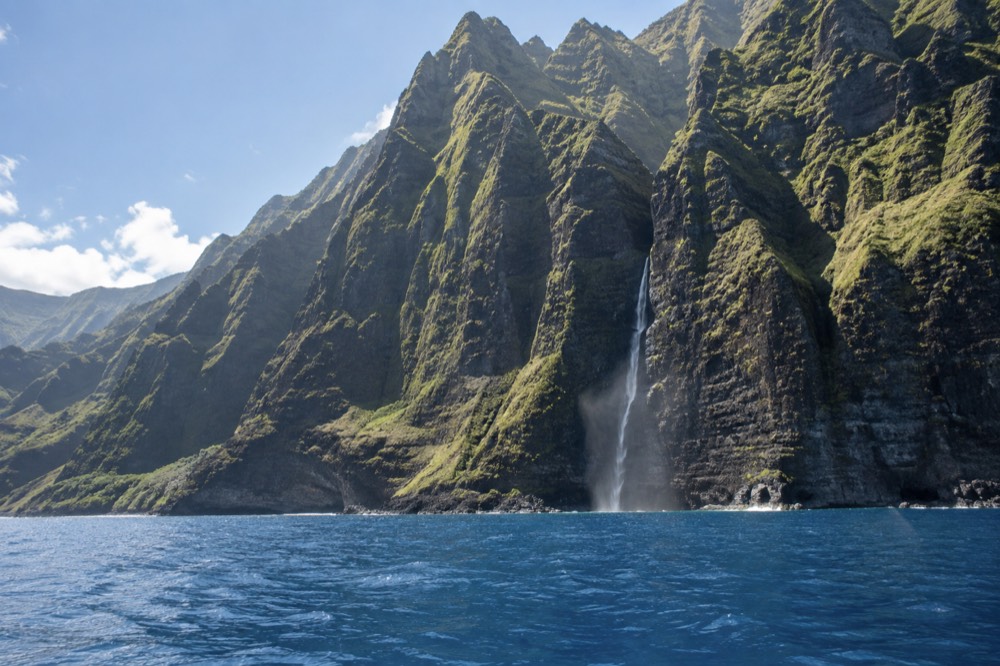 Tall green Napali sea cliffs rising directly from calm blue ocean water