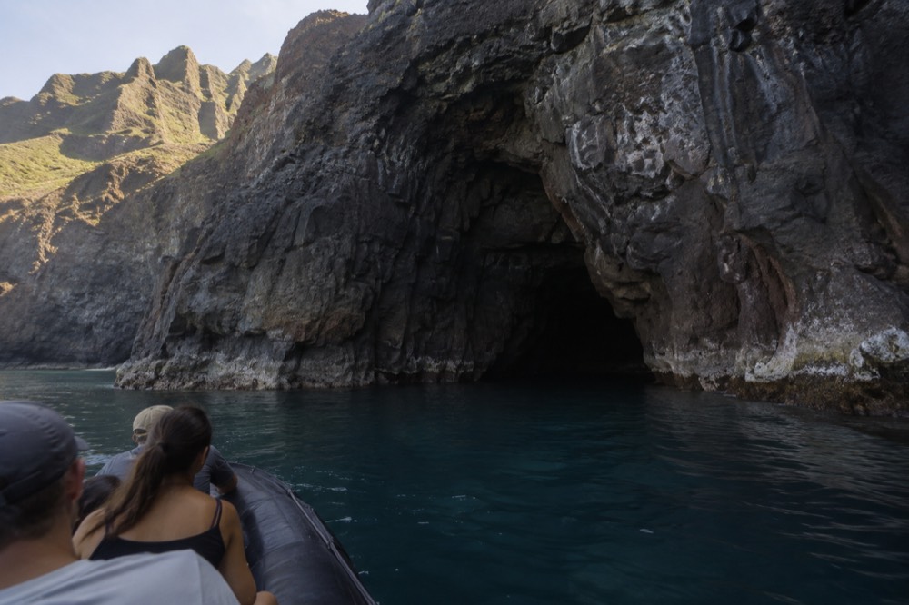 A small rigid inflatable raft floating just outside a dark sea cave opening in a cliff wall