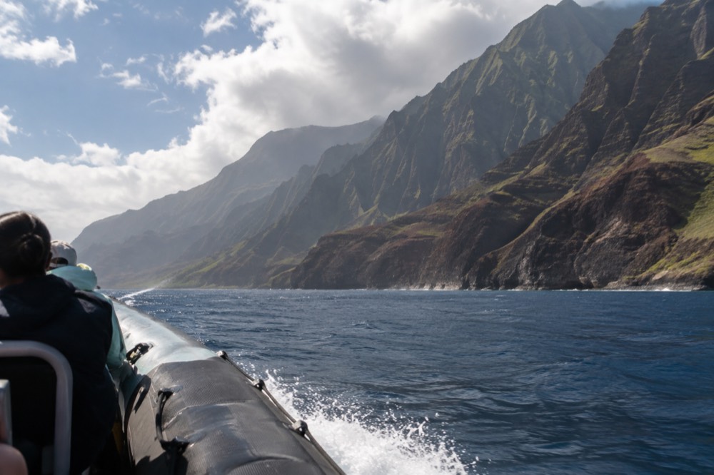 A raft traveling along a coastline of tall fluted cliffs under a partly cloudy sky