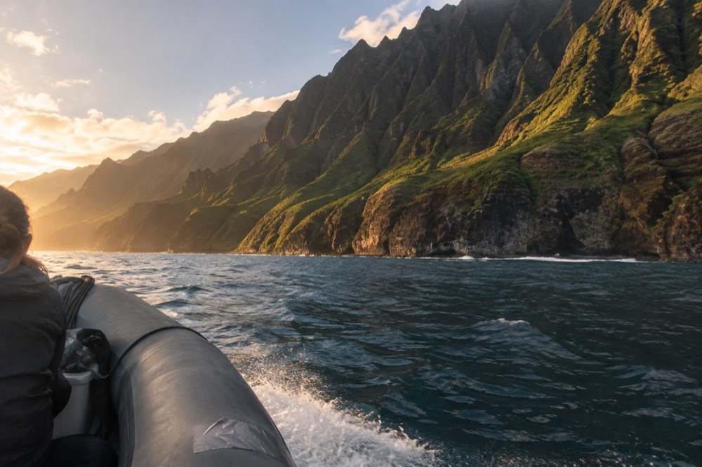 Rigid inflatable raft cruising close to a tall Napali cliff face