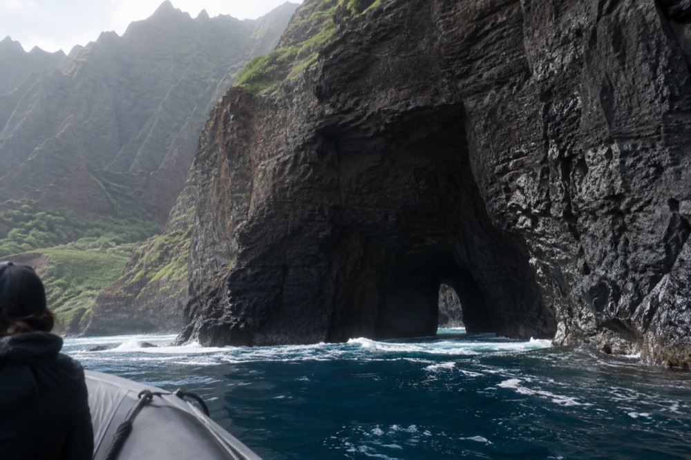 A small raft passing close to a dark sea cave entrance in a cliff face