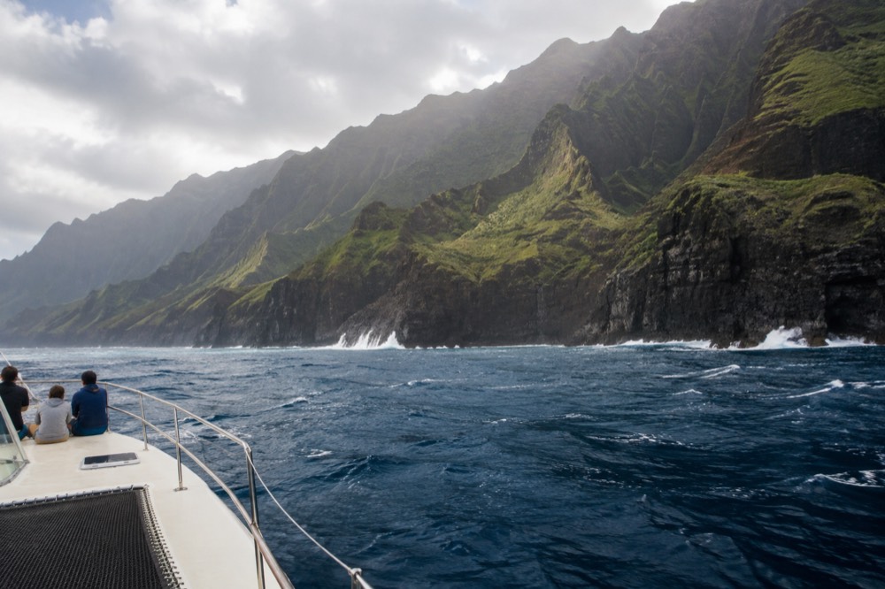 A power catamaran cruising past steep green sea cliffs on the Napali Coast