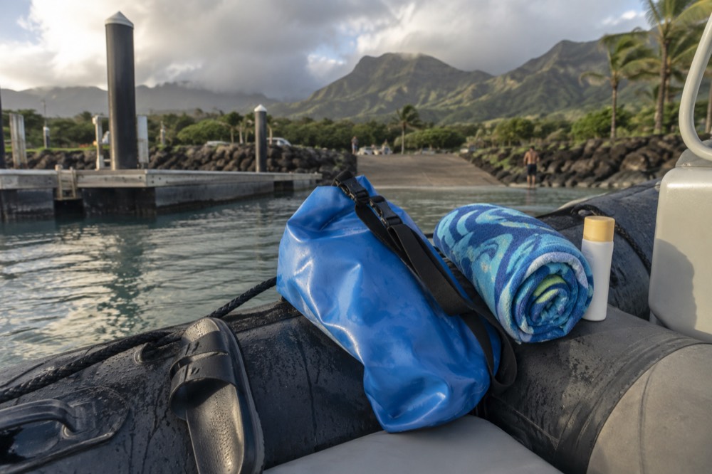 A dry bag and towel and sunscreen arranged on the tube side of a small boat
