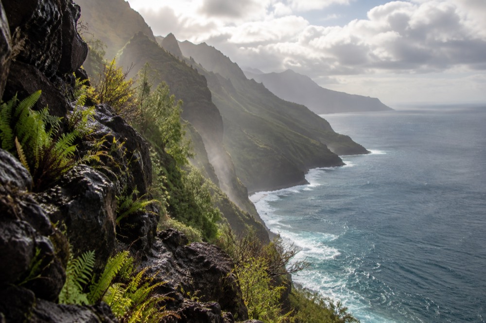 Green ridges of the Napali Coast dropping steeply into the Pacific Ocean under scattered clouds