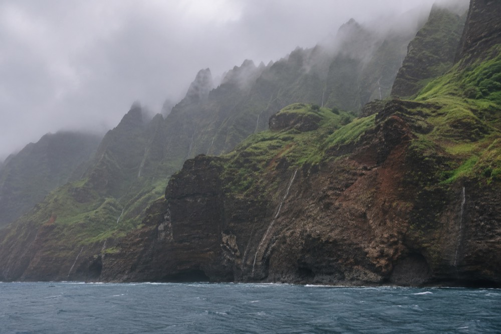 Towering green cliff face meeting the ocean with no visible road or building along the shoreline