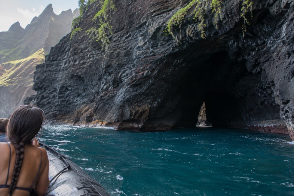 A rigid inflatable raft cruising close to a sea cliff with a cave opening