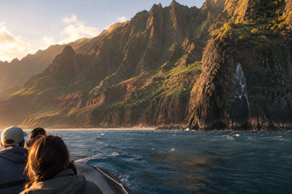 A small raft cruising close beneath towering fluted sea cliffs at golden hour