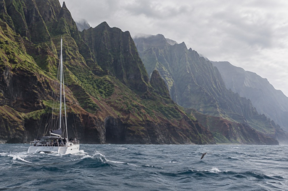 A catamaran under way near green sea cliffs on Kauai's southwest coast