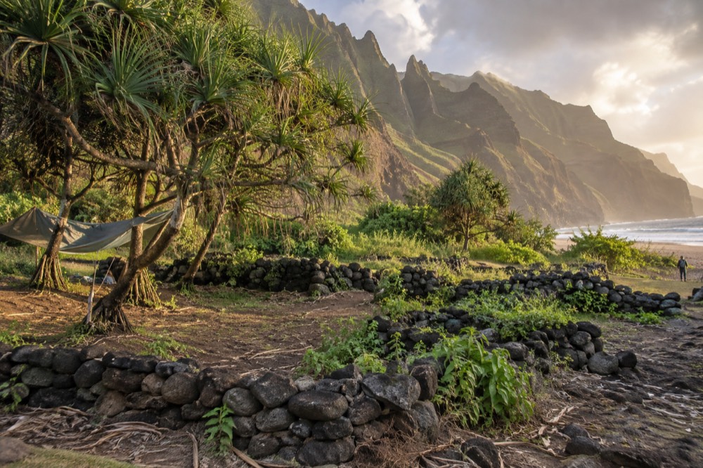 Low stacked stone terraces of the old Hawaiian settlement sit on the valley floor behind Kalalau Beach